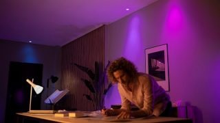 Una persona está inclinada sobre un escritorio en casa, en una habitación con iluminación ambiental colorida