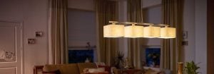 La moderna lámpara colgante LED con múltiples pantallas de tela ilumina una acogedora sala de estar, mostrando soluciones de iluminación doméstica energéticamente eficientes y elegantes para un confort de ambiente nocturno.