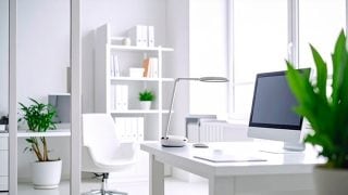 Una habitación blanca y luminosa muestra un escritorio con una computadora y una lámpara de mesa en él