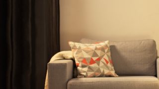 Acogedora sala de estar con una moderna luminaria de sobremesa LED, que ilumina el sillón para dos gris y crea un ambiente cálido para relajarse en casa.