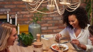Cocina moderna con luminarias colgantes LED de estilo vintage que iluminan a dos mujeres que disfrutan de la cena, creando un ambiente cálido y acogedor.